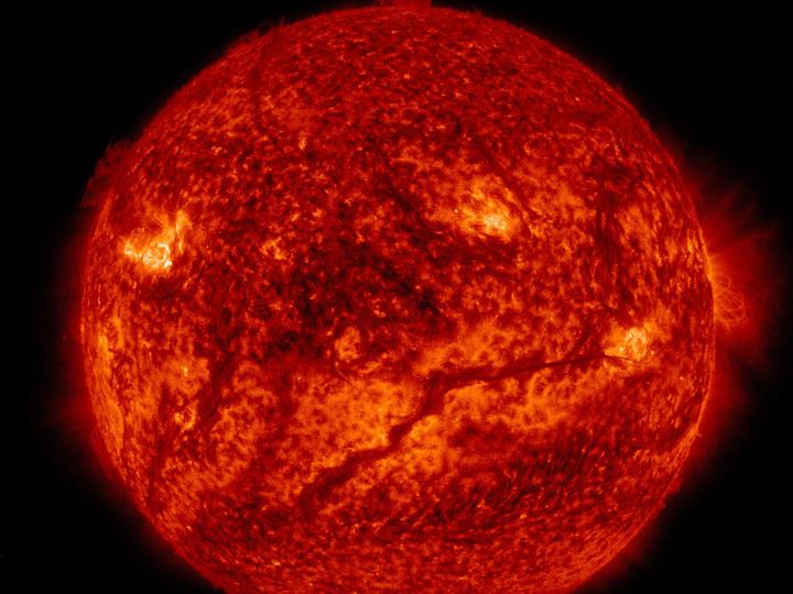 The Sun in extreme ultraviolet light, glowing gold with a long dark filament snaking across its lower half